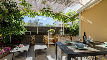 Ulkoterassi, jossa on ruokailuryhmä, pehmustetut istuimet ja köynnöskasveilla koristeltu pergola.