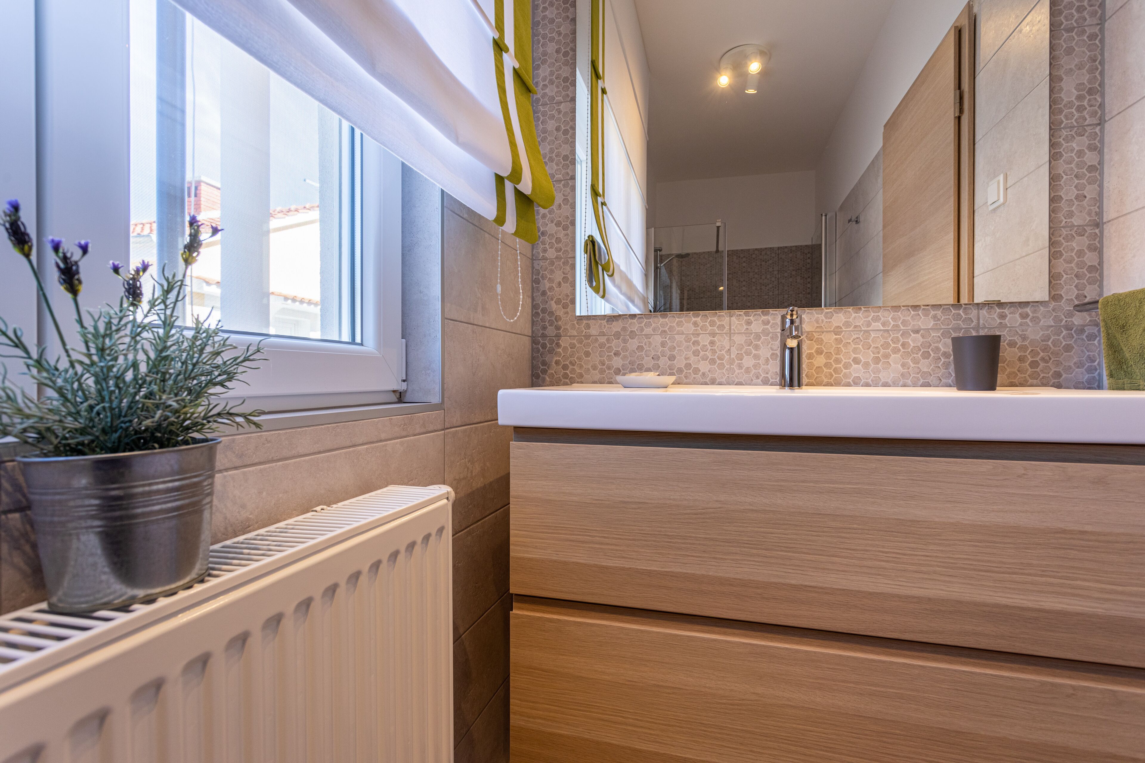 Een moderne badkamer met een raam, pot lavendel, een witte radiator en houten kastjes.
