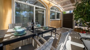 Un patio al aire libre con una mesa de comedor preparada para dos personas, rodeado de sillas de mimbre.