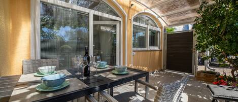 An outdoor patio with a dining table set for two, surrounded by wicker chairs.