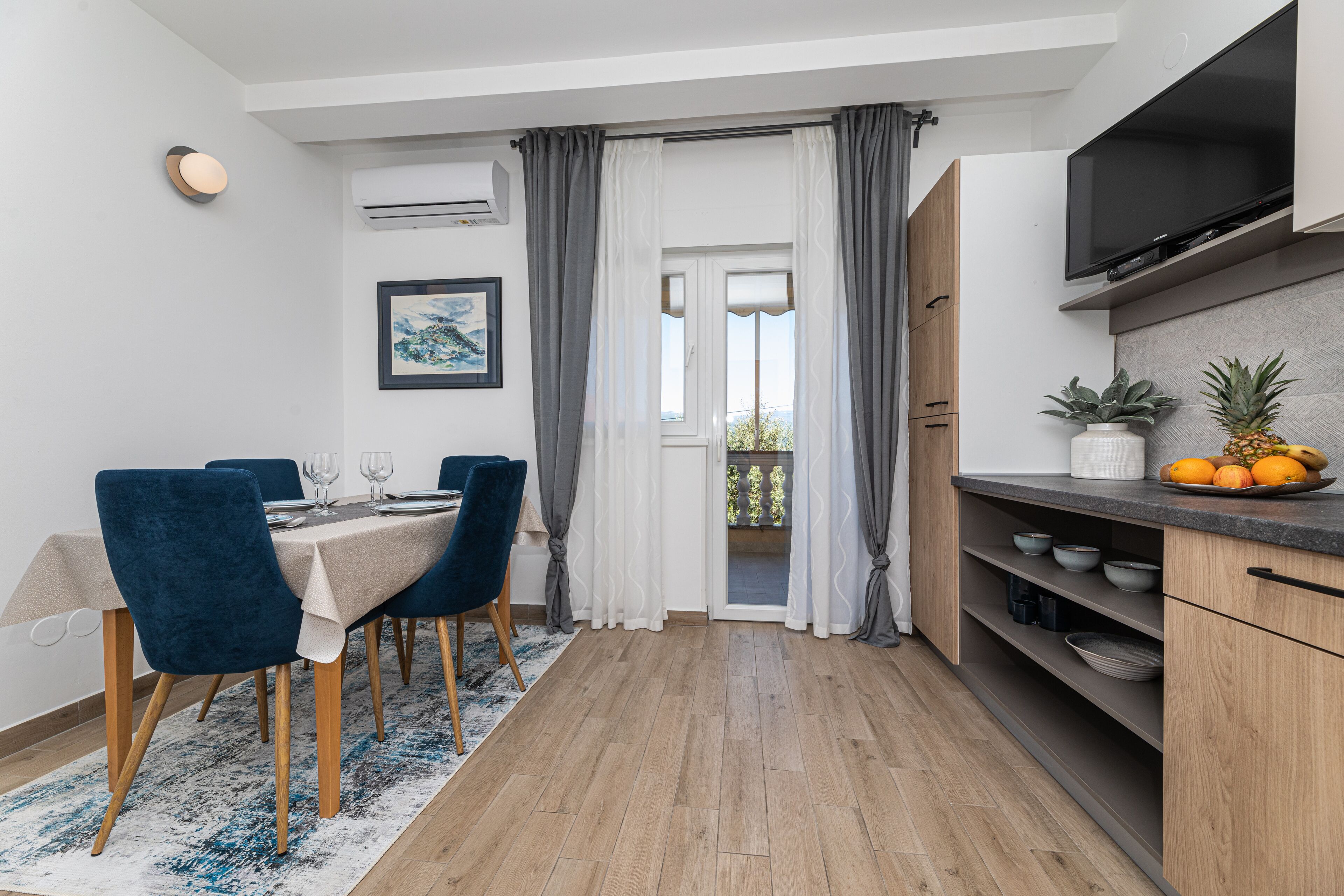A modern kitchen with a built-in TV, wooden cabinets, and a dining area with blue chairs and a table.