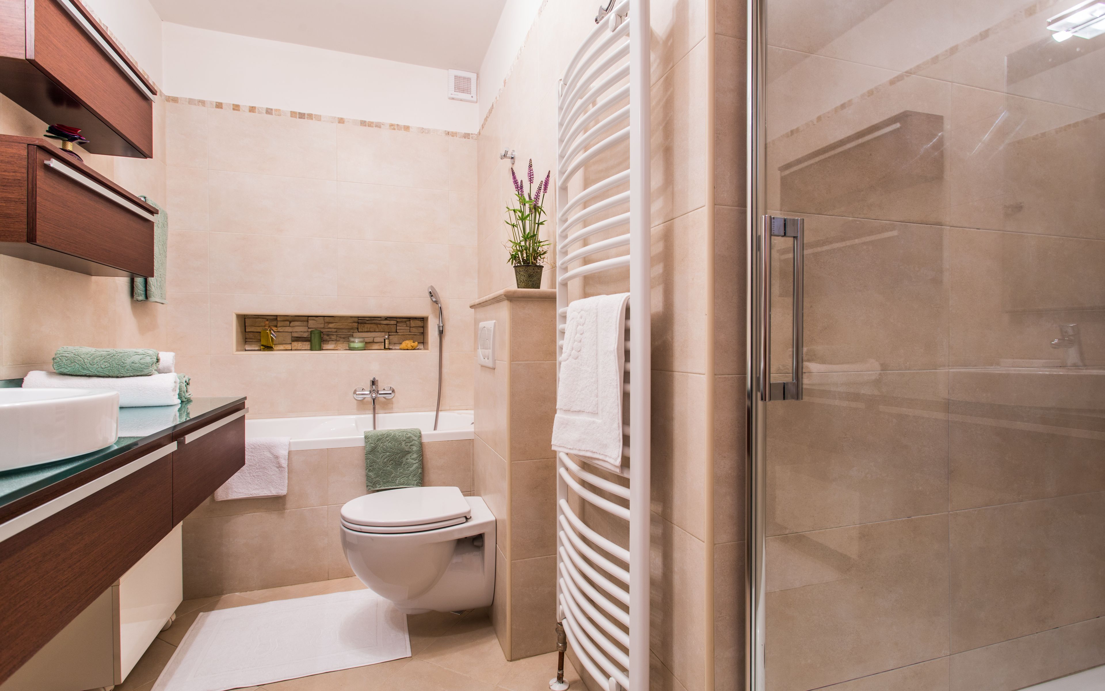 A modern bathroom with a bathtub, toilet, and shower. There is a vanity with a sink and a mirror. A towel is hanging on the wall.