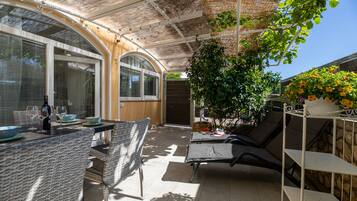 En overdækket terrasse med fletningsmøbler, et bord dækket med vinglas og en potteplante.