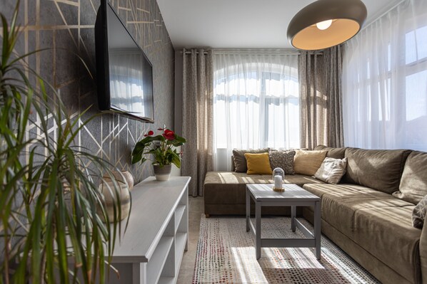 Una sala de estar moderna con un sofá, una mesa de centro, un televisor montado en la pared y una planta en maceta.