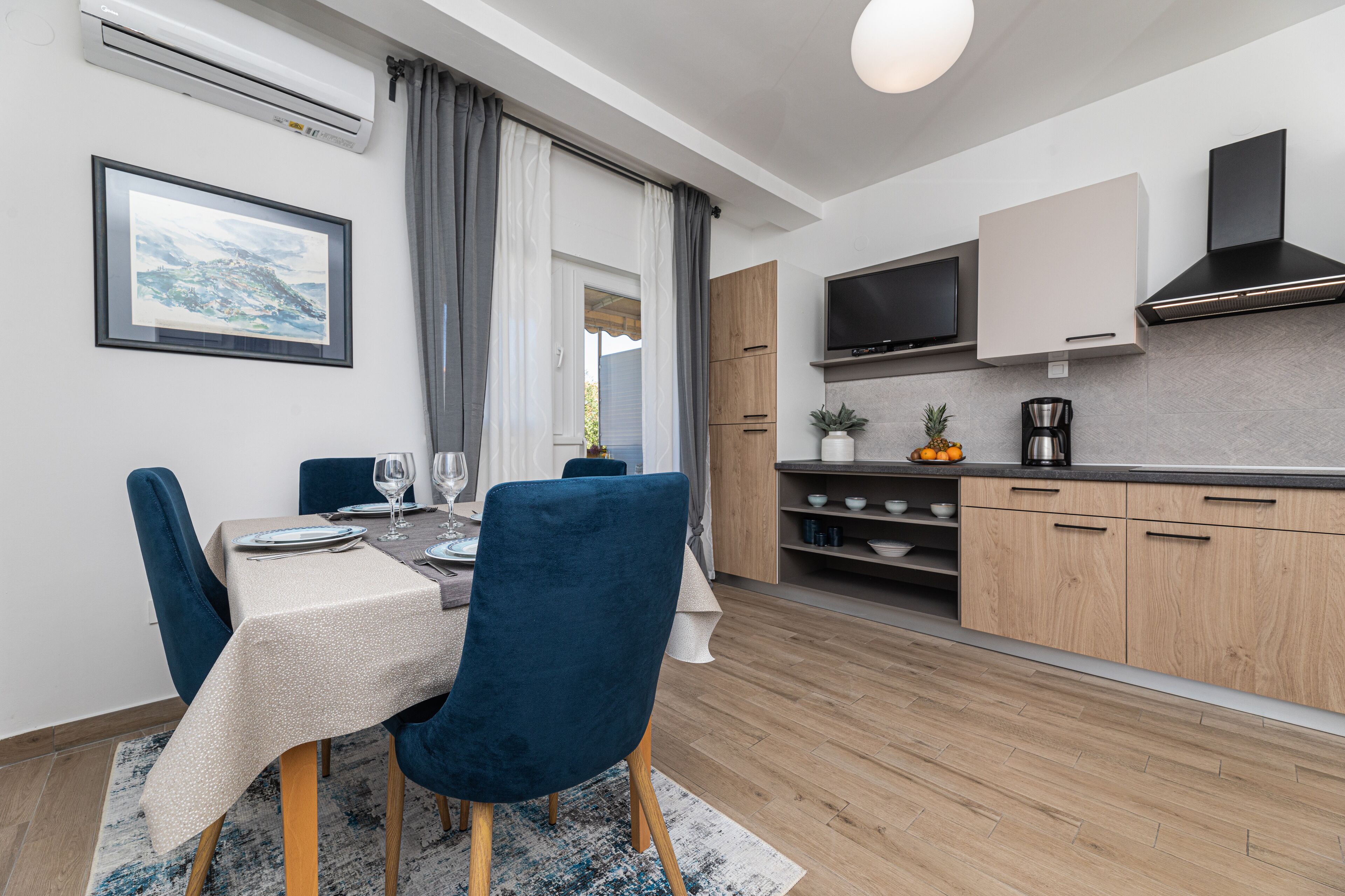 Een moderne keuken met een flatscreen televisie, houten kastjes en een koffiezetapparaat.