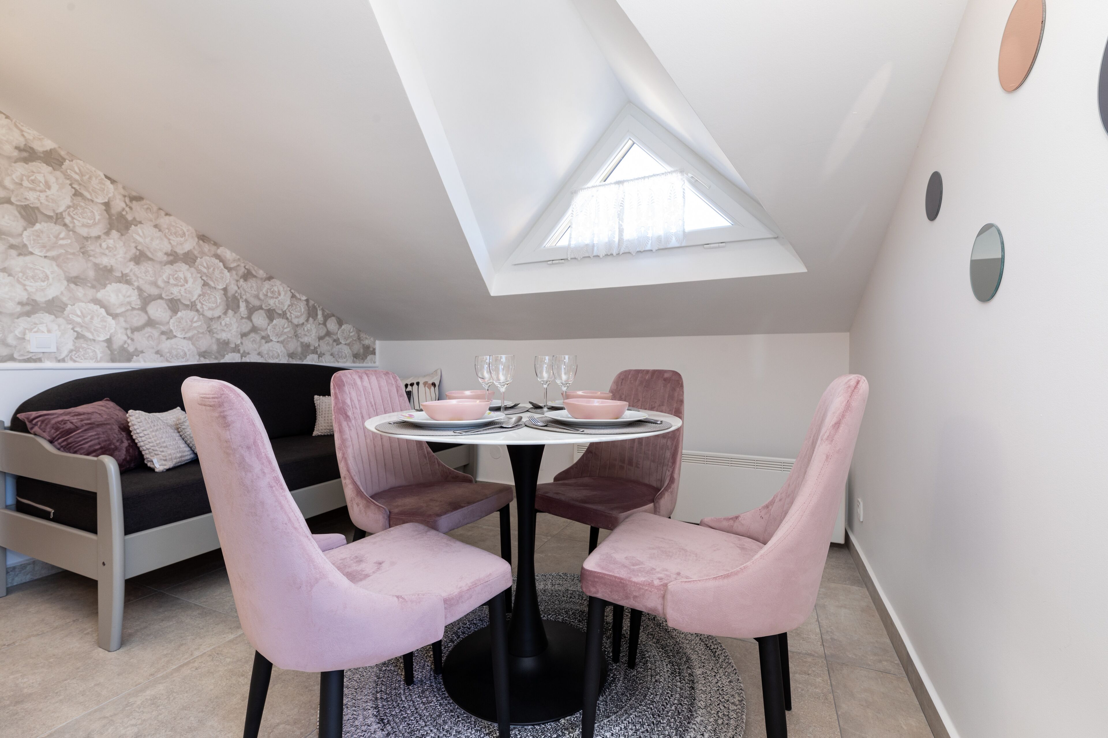 A modern loft bedroom with a skylight, a black sofa, pink chairs, and a round dining table.