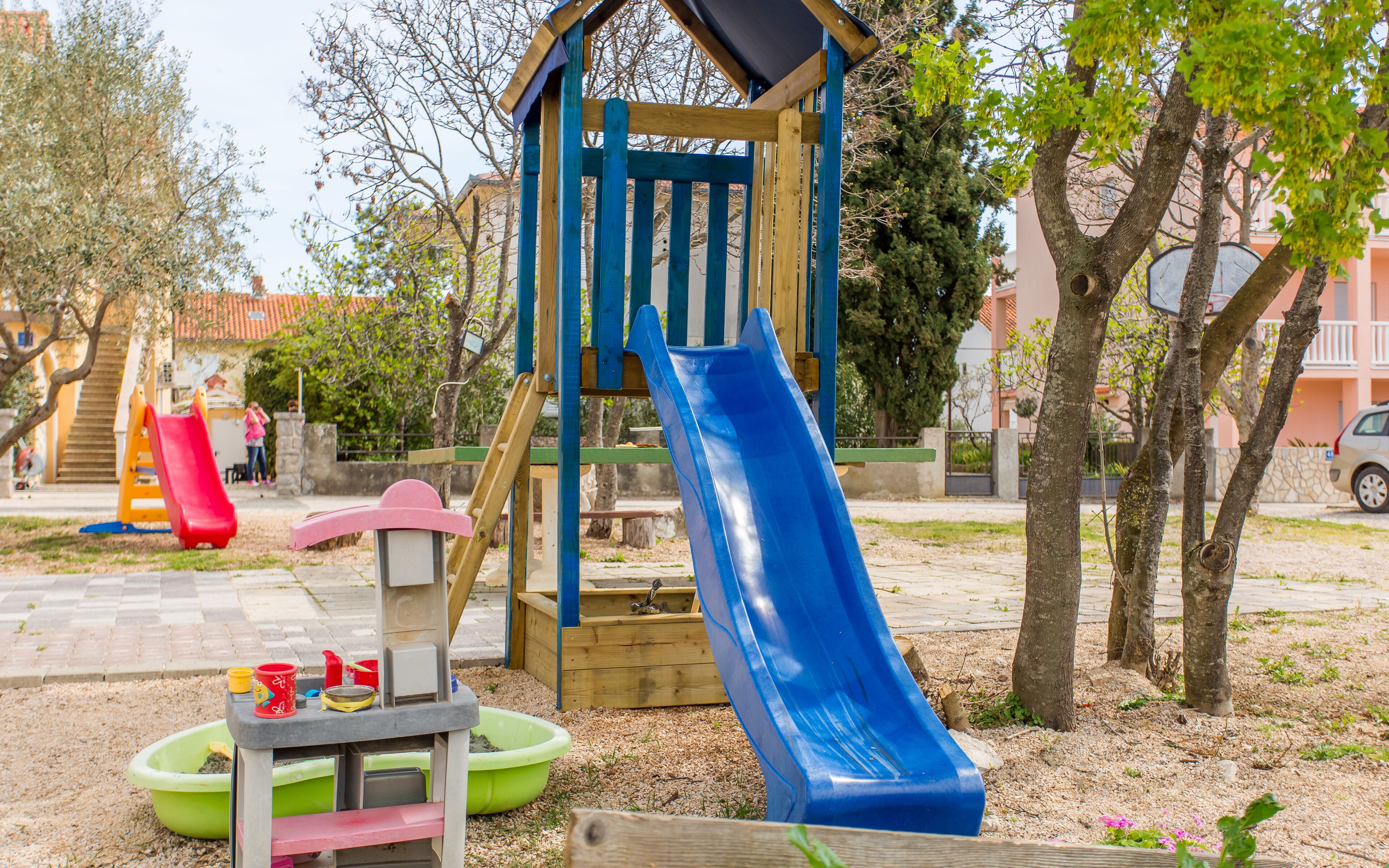 Une aire de jeux avec un toboggan bleu, un toboggan rouge et une structure d’escalade en bois.