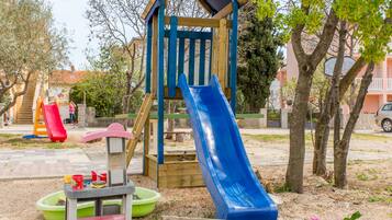 Une aire de jeux avec un toboggan bleu, un toboggan rouge et une structure d’escalade en bois.