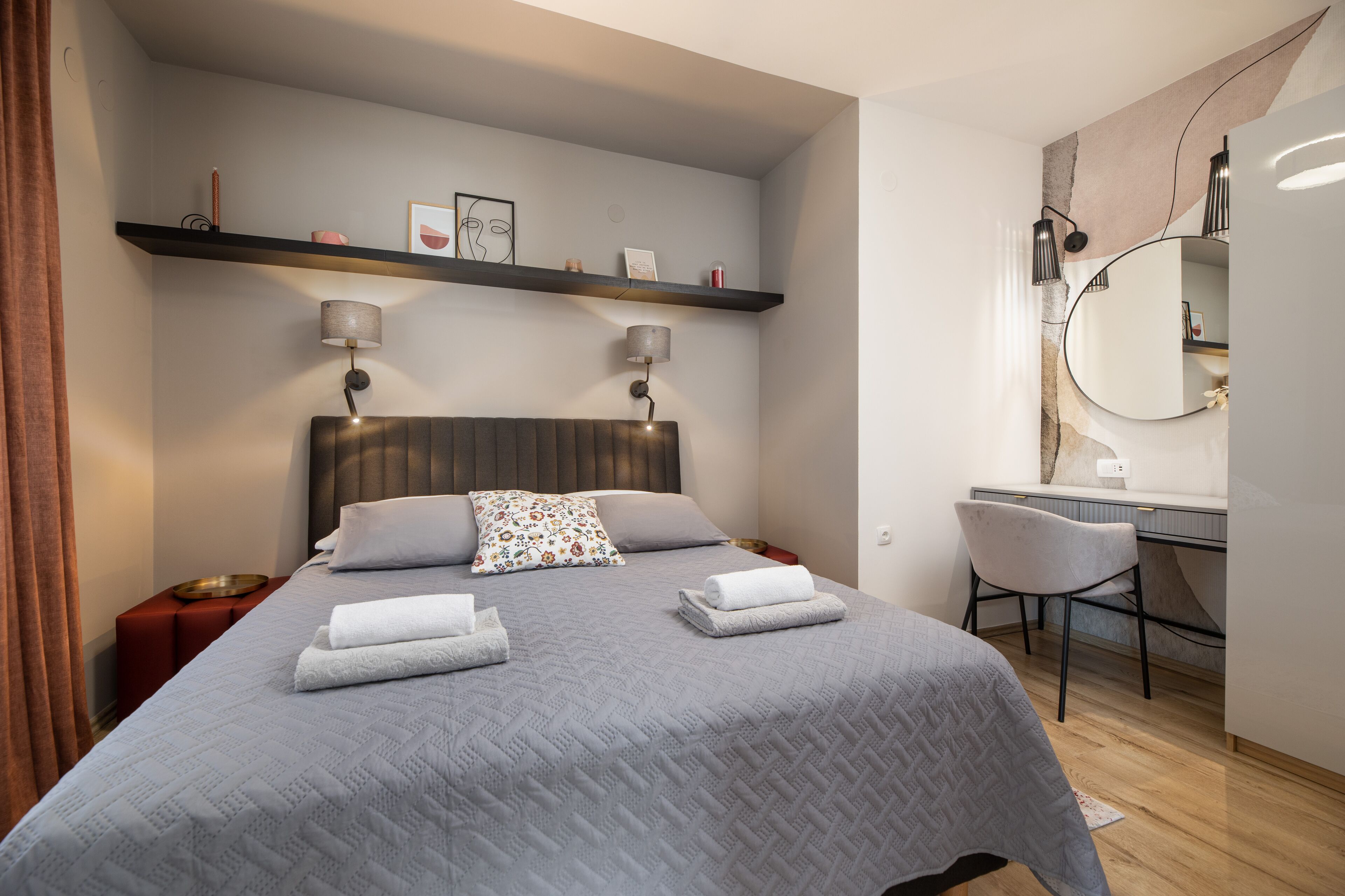 A modern hotel room with a neatly made bed, a desk with a chair, and a large mirror.