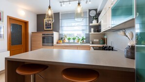 Una cocina moderna con una isla central, taburetes de bar, luces colgantes y vistas al exterior.