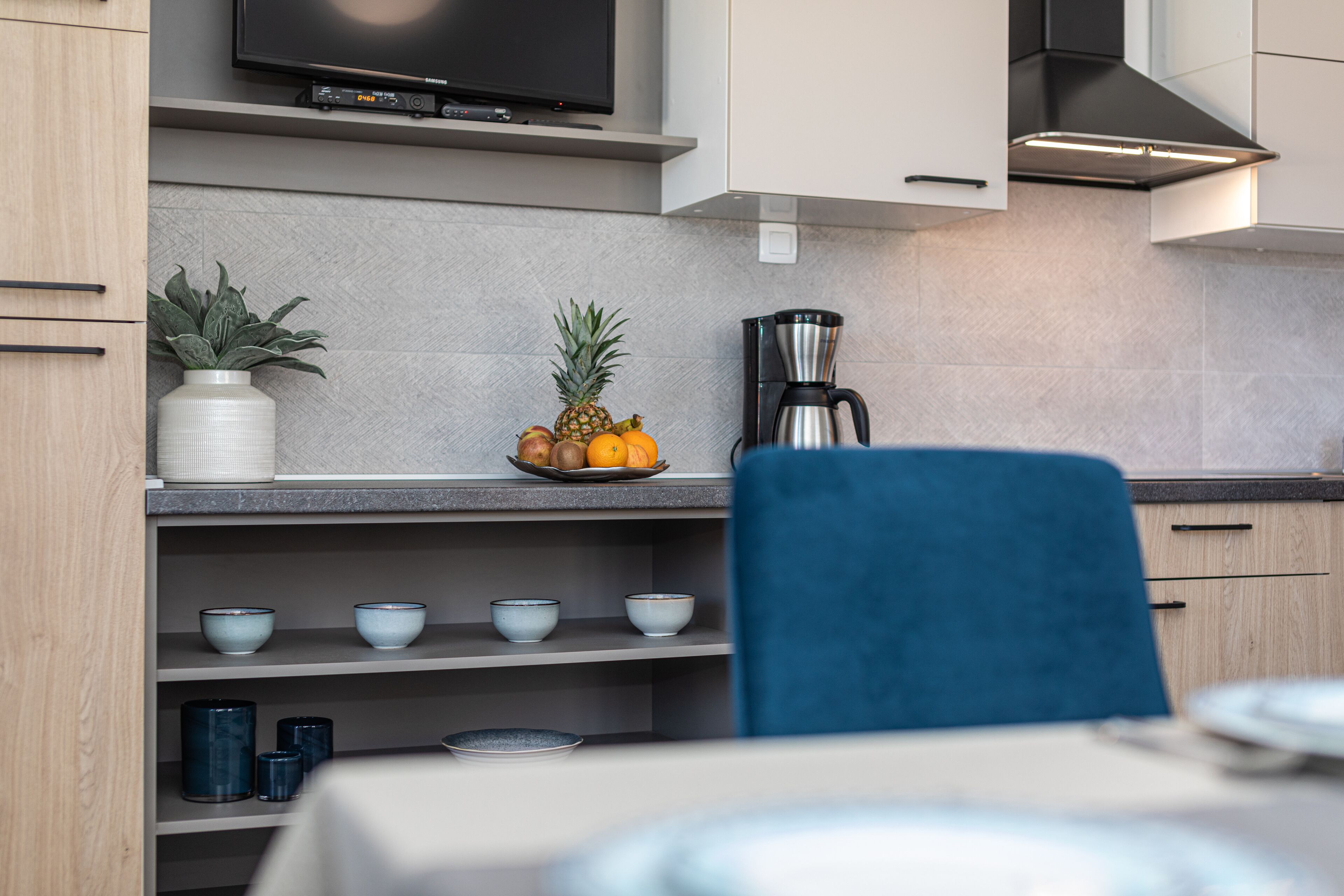 A modern kitchen with a flat-screen TV, a coffee maker, and a fruit bowl on the counter.