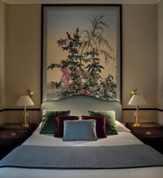 Una camera d'albergo con un letto grande, due comodini illuminati da lampade e un grande quadro floreale appeso al muro.