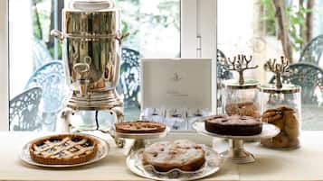A table with various desserts and a coffee pot, with a window and chairs in the background.