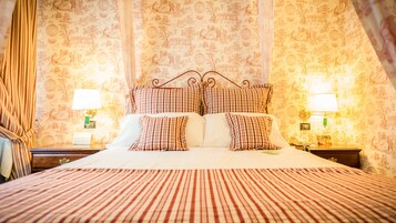 Un lit bien fait, recouvert d’une couvre-lit à rayures, avec une tête de lit décorative et des coussins assortis. On y trouve deux tables de chevet avec des lampes, et un mur recouvert d’un papier peint à motifs.