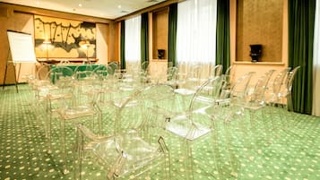 A conference room with clear plastic chairs arranged in rows, a green patterned carpet, and a whiteboard in the background.