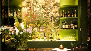 Eine Bar mit Regalen voller Spirituosenflaschen und Gläsern, einer Blumenvase und einem dekorativen Wandgemälde.