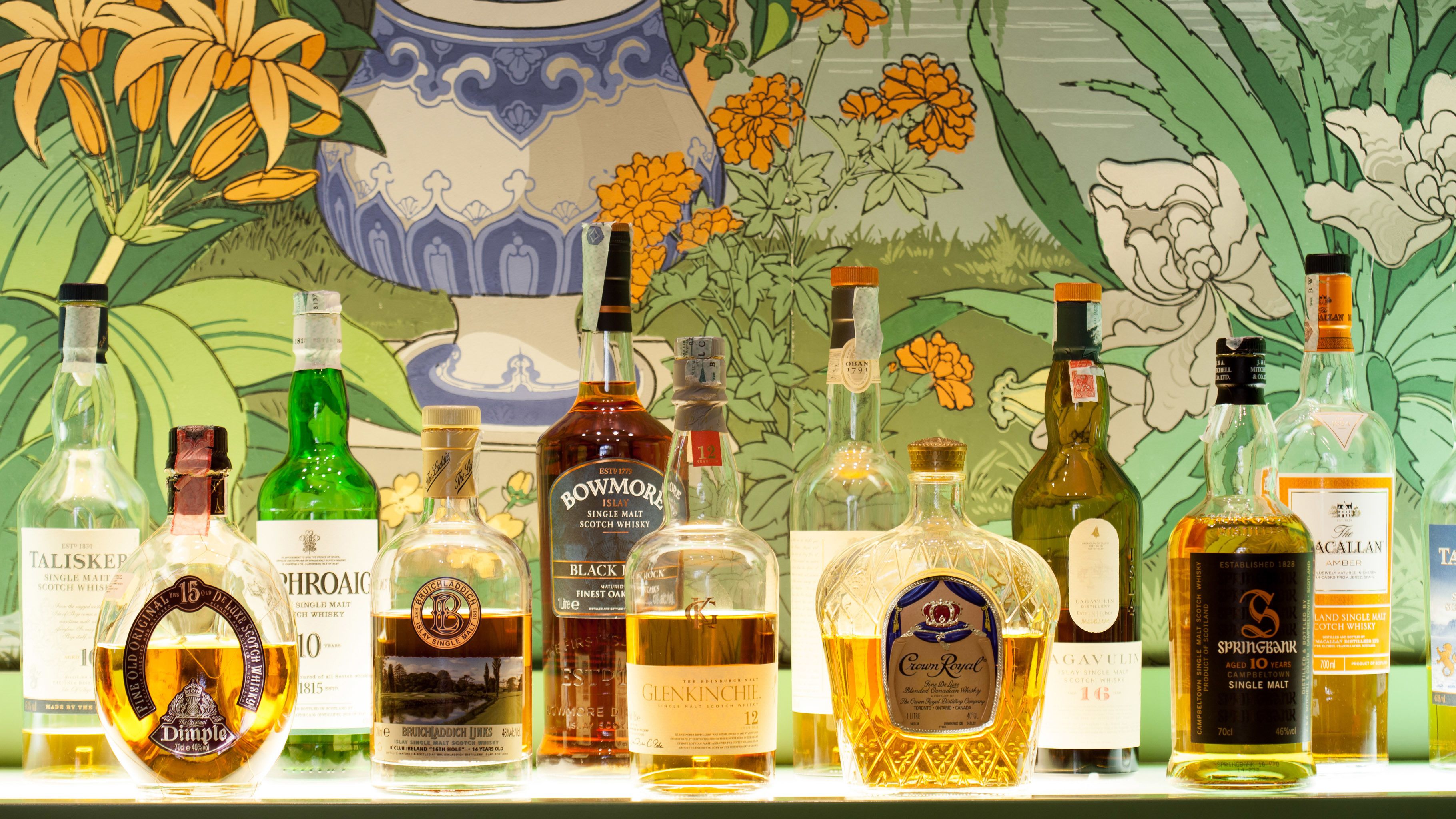 Varias botellas de whisky exhibidas en una estantería frente a un fondo decorativo.