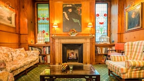 Ein gemütlicher Raum mit Kamin, Sofas mit Blumenmuster, einem gestreiften Sessel und einem Bücherregal voller Bücher.
