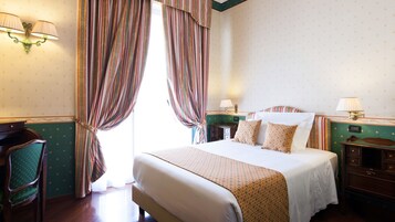 Una camera d'albergo con un letto grande, due comodini, una scrivania, una sedia e tende.