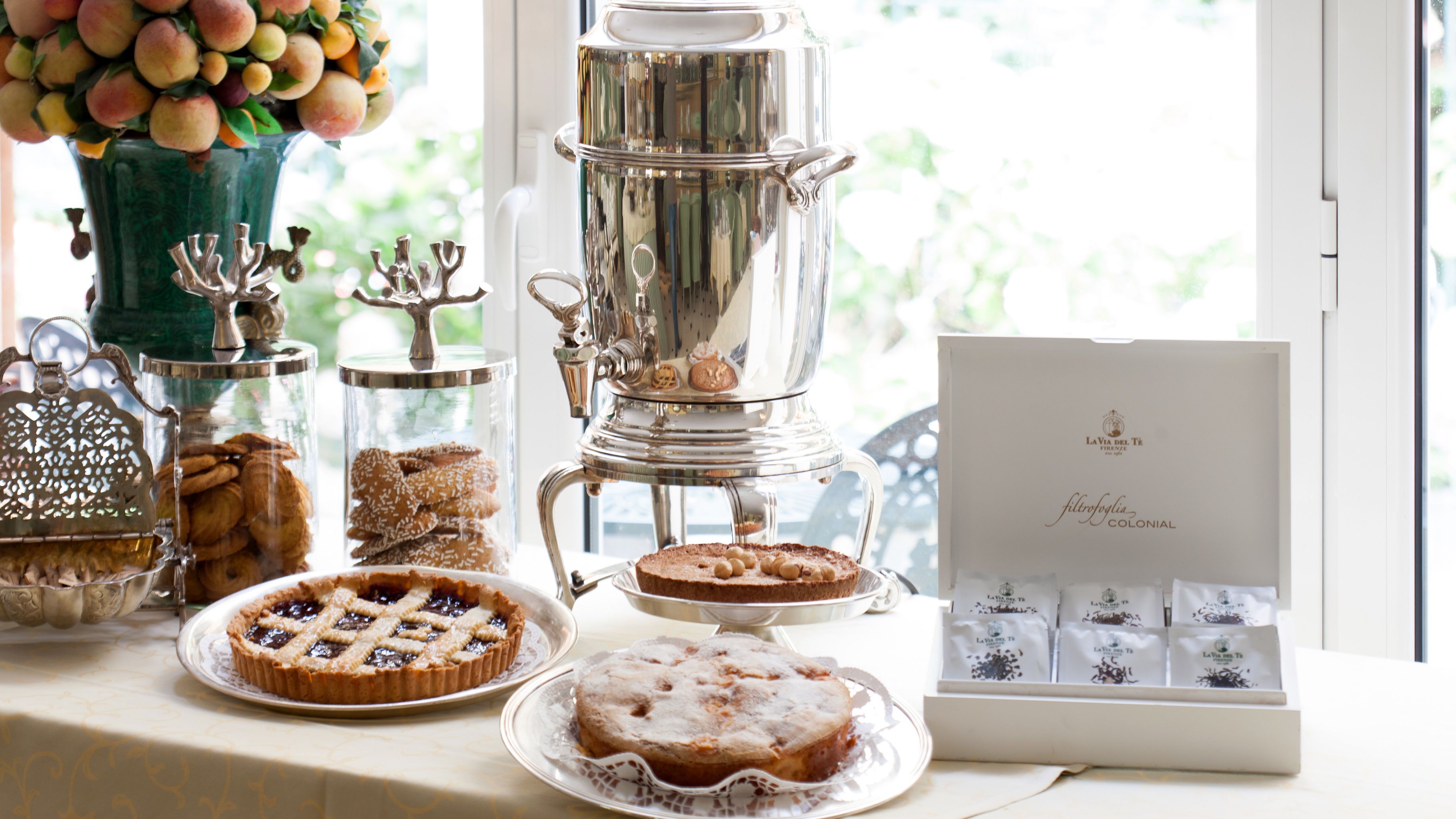 Una mesa con diferentes alimentos, incluyendo tartas y pasteles, además de una máquina de café.