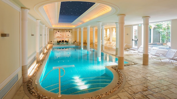 Ein großes Hallenbad mit Sternenhimmel, umgeben von Säulen und Liegestühlen.