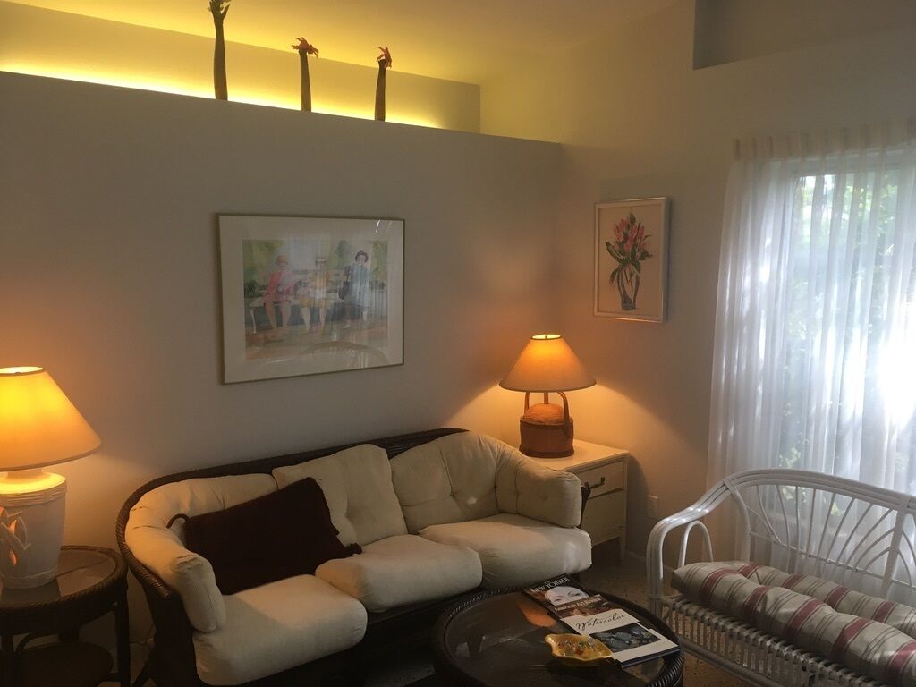 Un salon comprenant un canapé, un fauteuil, une table basse et deux lampes. Des tableaux encadrés ornent le mur.