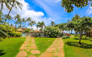 Ein tropisches Resort mit einem gepflasterten Weg, der zu einem Pool führt, umgeben von Palmen und üppiger Vegetation.