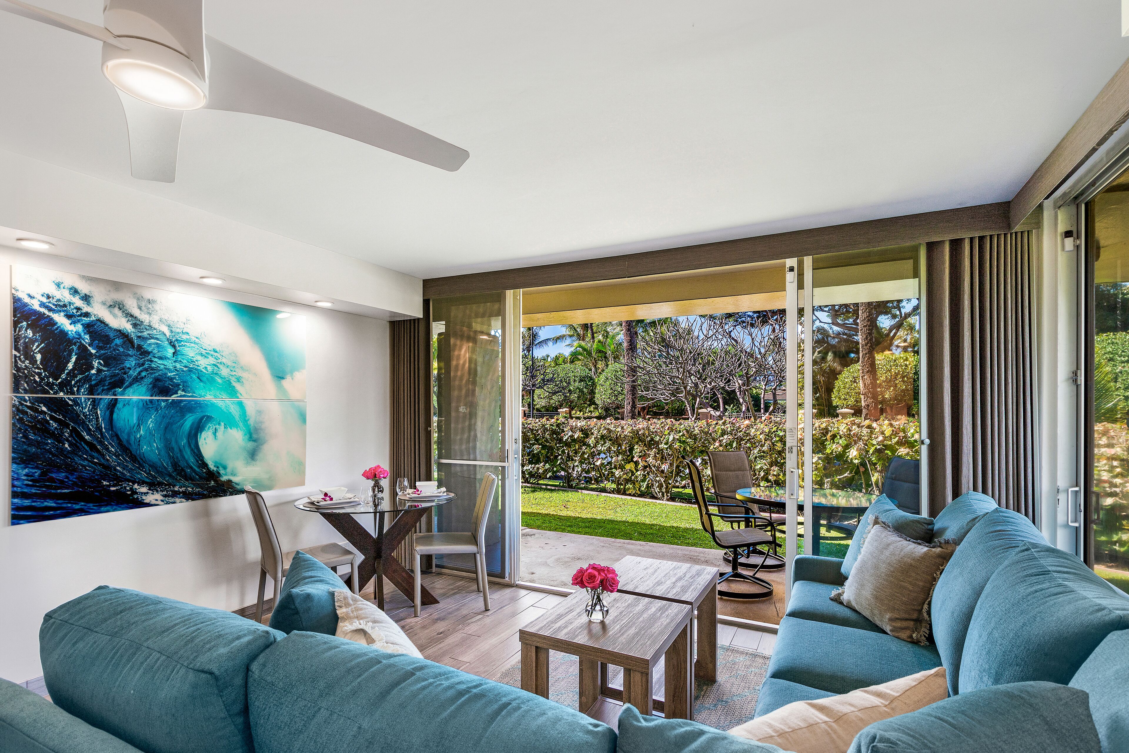 A modern living room with a large window, a ceiling fan, a dining area, and a garden view.