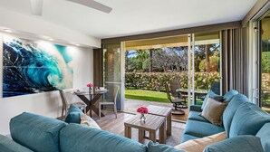 Una sala de estar moderna con un ventanal grande, ventilador de techo, comedor y vista a un jardín.