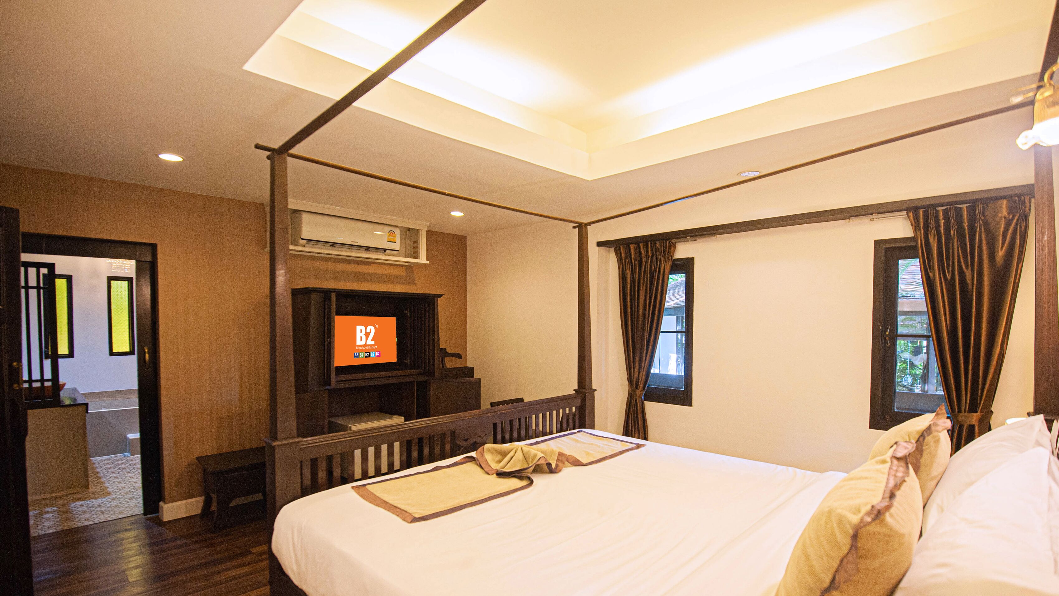 Ein Hotelzimmer mit einem großen Bett, einem an der Wand befestigten Fernseher und Blick ins Freie durch das Fenster.