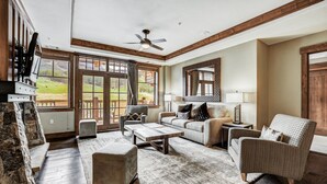 A spacious living room with a fireplace, comfortable seating, and large windows offering a view of the outdoors.