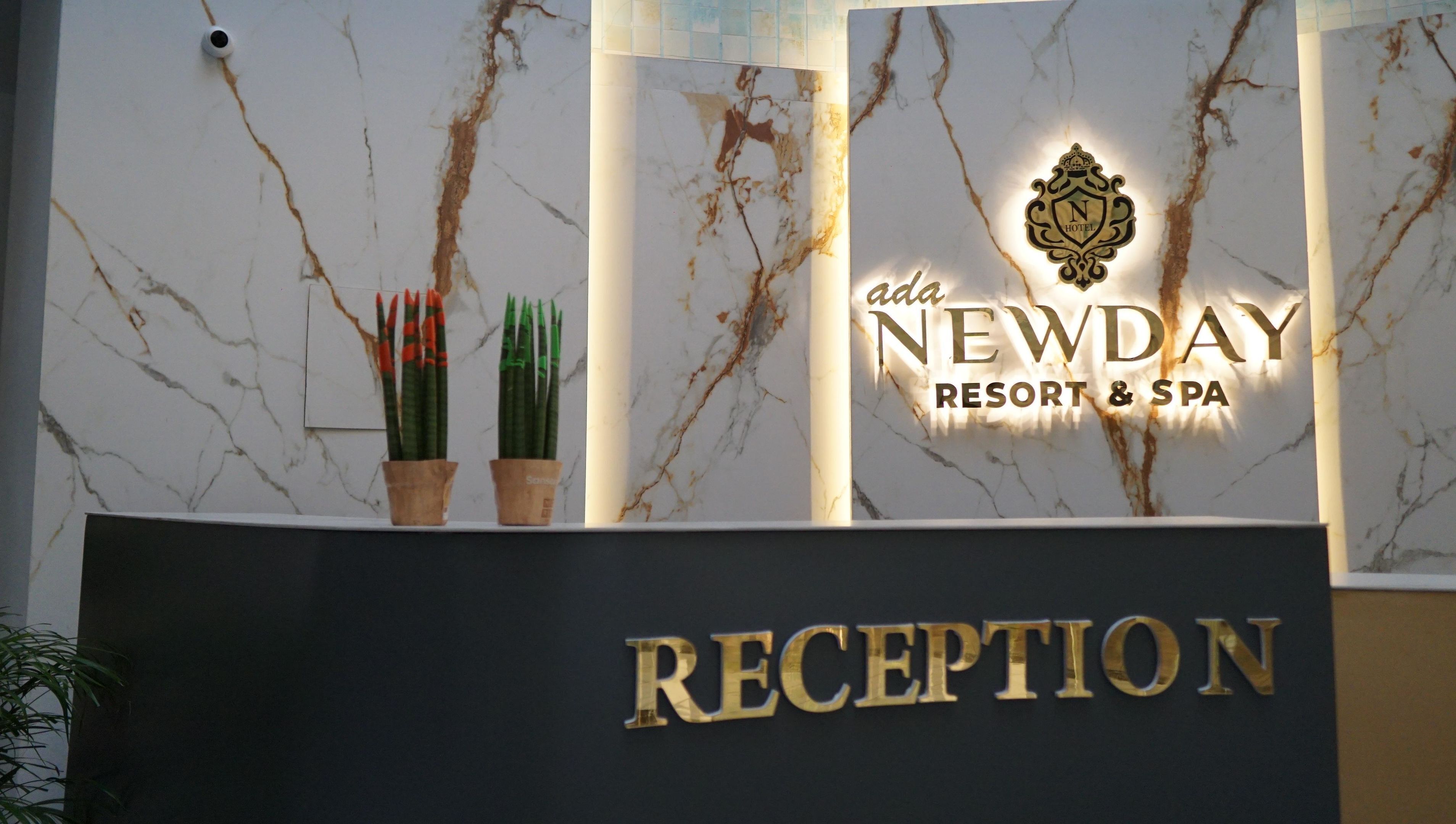 A reception desk with a marble design, two potted plants, and a sign for 'Newday Resort & Spa'.