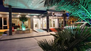 A modern hotel entrance with a well-lit reception area, a landscaped garden with a tree, and a BMW car parked outside. - Ada Newday Resort Hotel (Kusadasi)