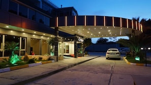 A hotel entrance with a covered walkway, a car parked in front, and well-lit outdoor areas with plants.