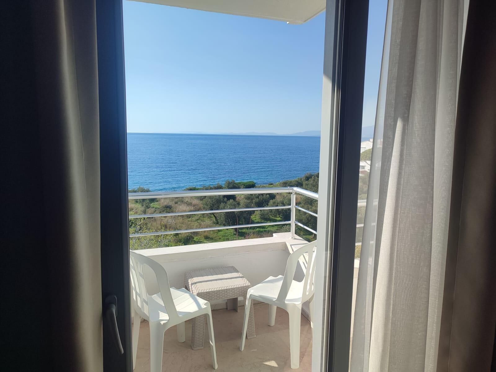Un balcón con vista al mar, sillas de plástico blanco y una mesita.