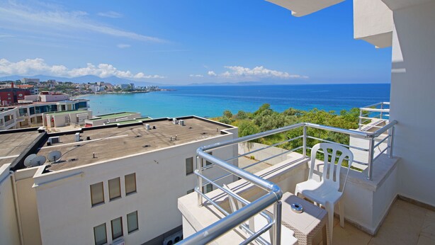 Ein Balkon mit Blick auf das Meer, weiße Gebäude und einen klaren Himmel.