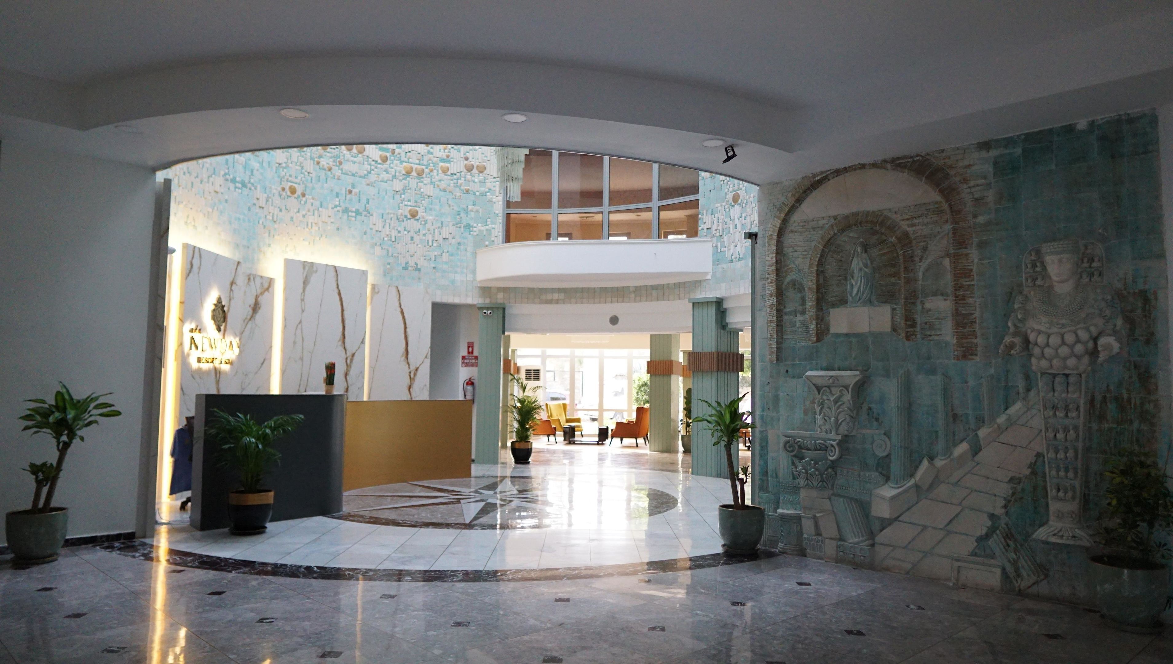A spacious lobby with a high ceiling, a reception desk, and a mural on the wall.