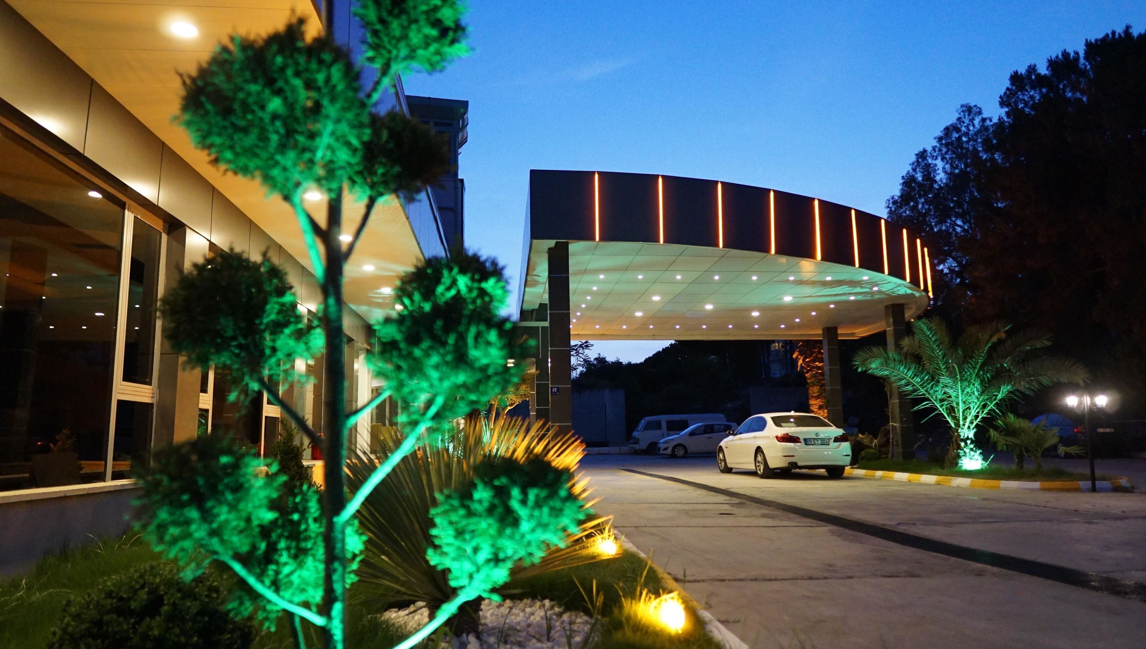 A modern hotel entrance with a covered driveway, a white car parked inside, and illuminated greenery.