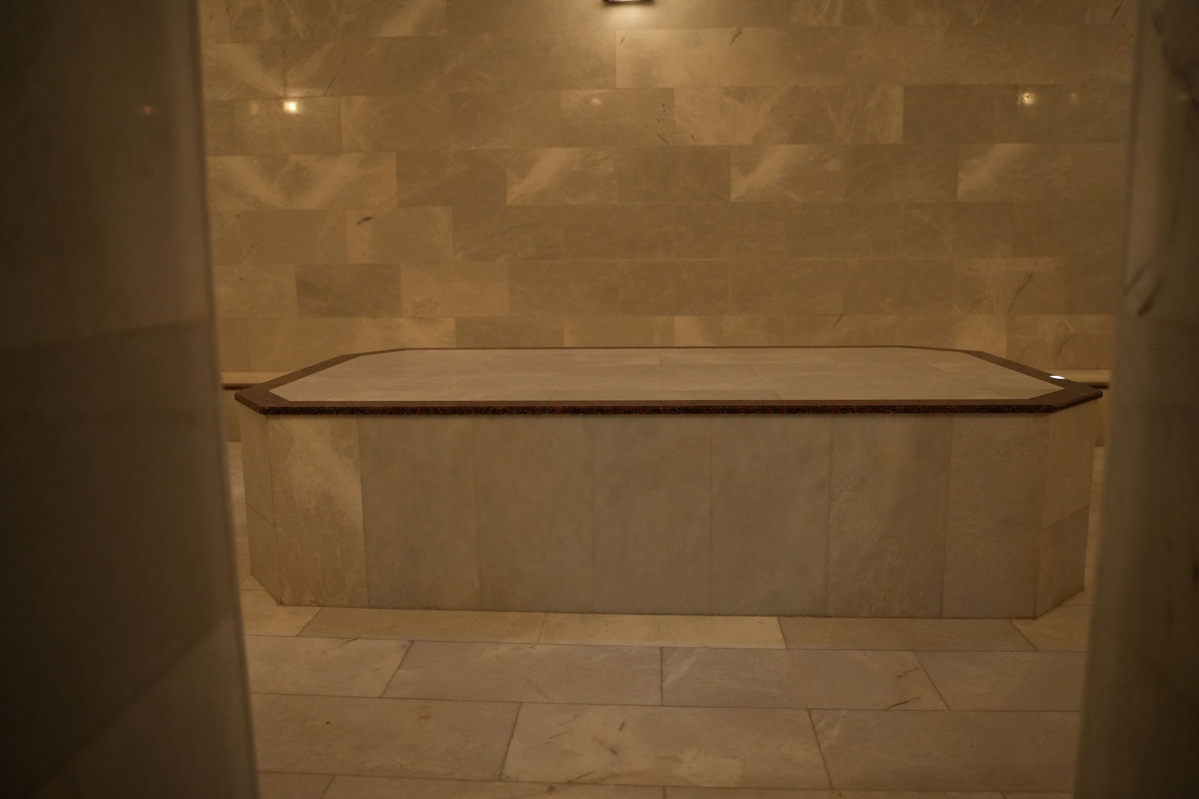 A bathroom with a marble wall and floor, a wooden countertop, and a shower area.