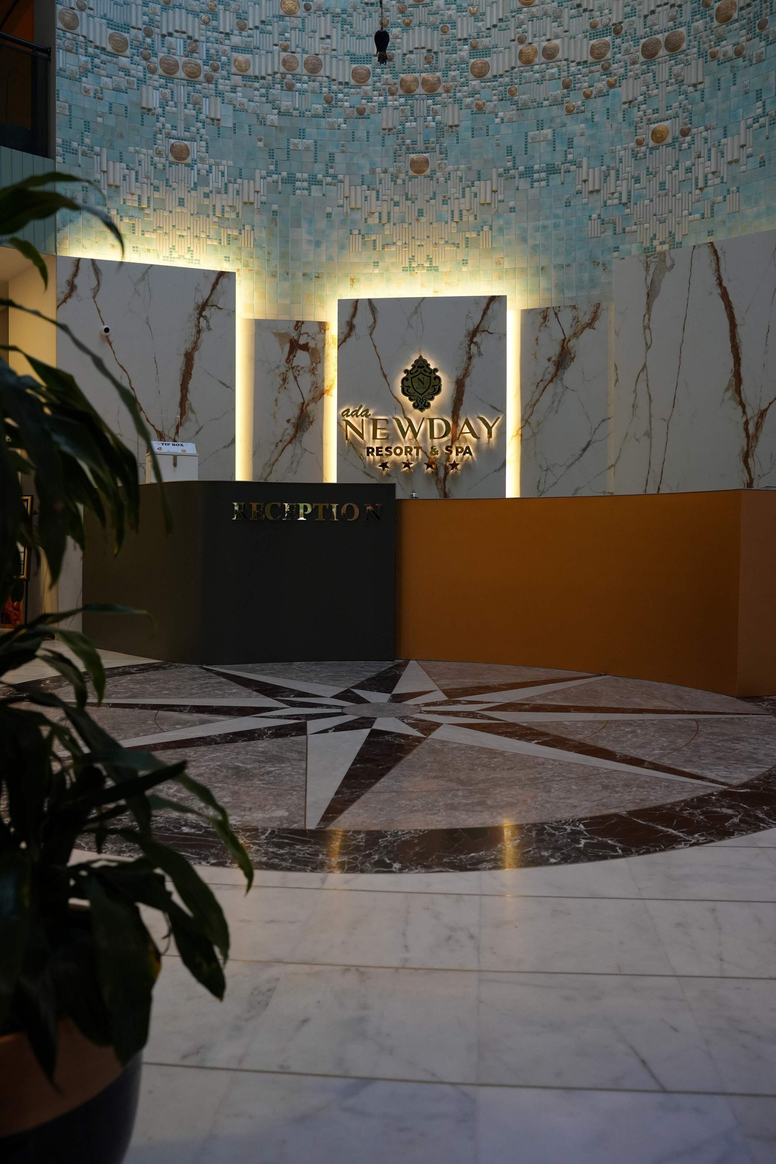 Un espace d’accueil doté d’un sol en marbre, d’un mur orné d’un motif géométrique et d’une enseigne indiquant « NEDAY Resort & Spa ».