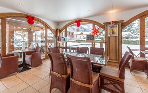A restaurant with wicker chairs and tables, large windows with wooden frames, and a menu board. - Hotel L'Oustalet (Chamonix-Mont-Blanc)