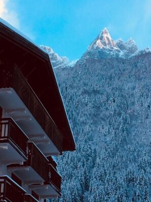 A wooden building with multiple balconies, set against a backdrop of snow-covered mountains and clear blue sky. - Hotel L'Oustalet (Chamonix-Mont-Blanc)