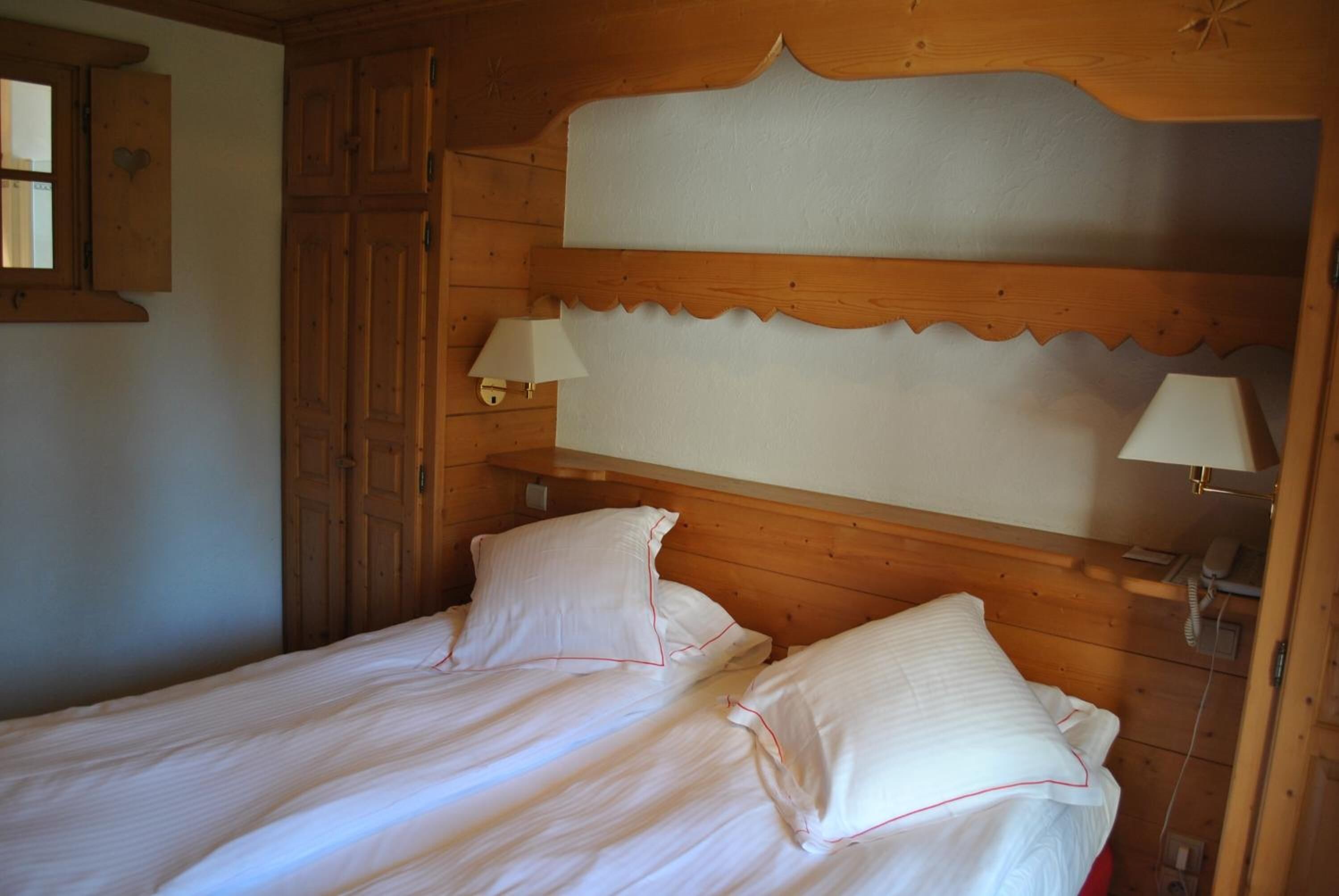 A wooden room with a bed, two bedside lamps, and a wooden wardrobe.