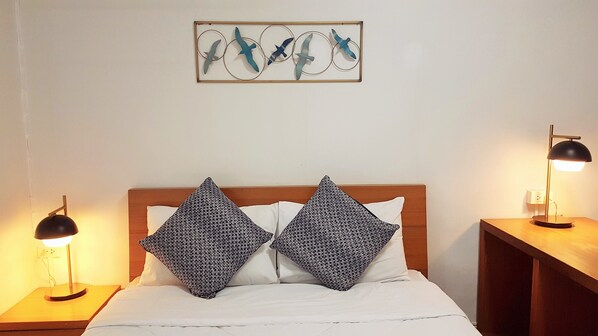 Una cama bien hecha con almohadones estampados, un cabecero de madera y dos lámparas de noche.