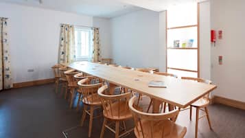 A conference room with a long wooden table and chairs, a window with curtains, and a bookshelf with books.