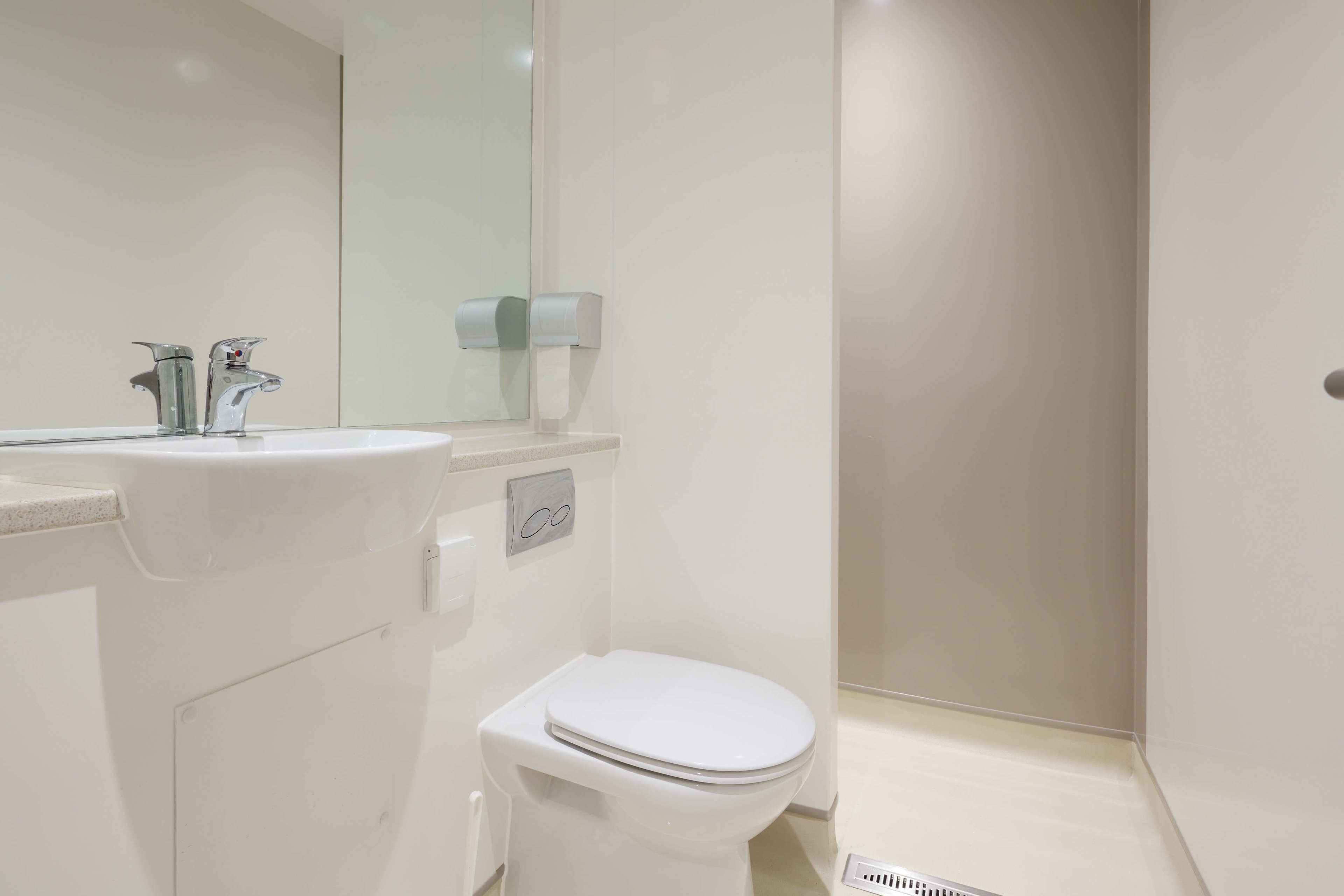 A modern bathroom with a white sink, a mirror, a toilet, and a towel dispenser.