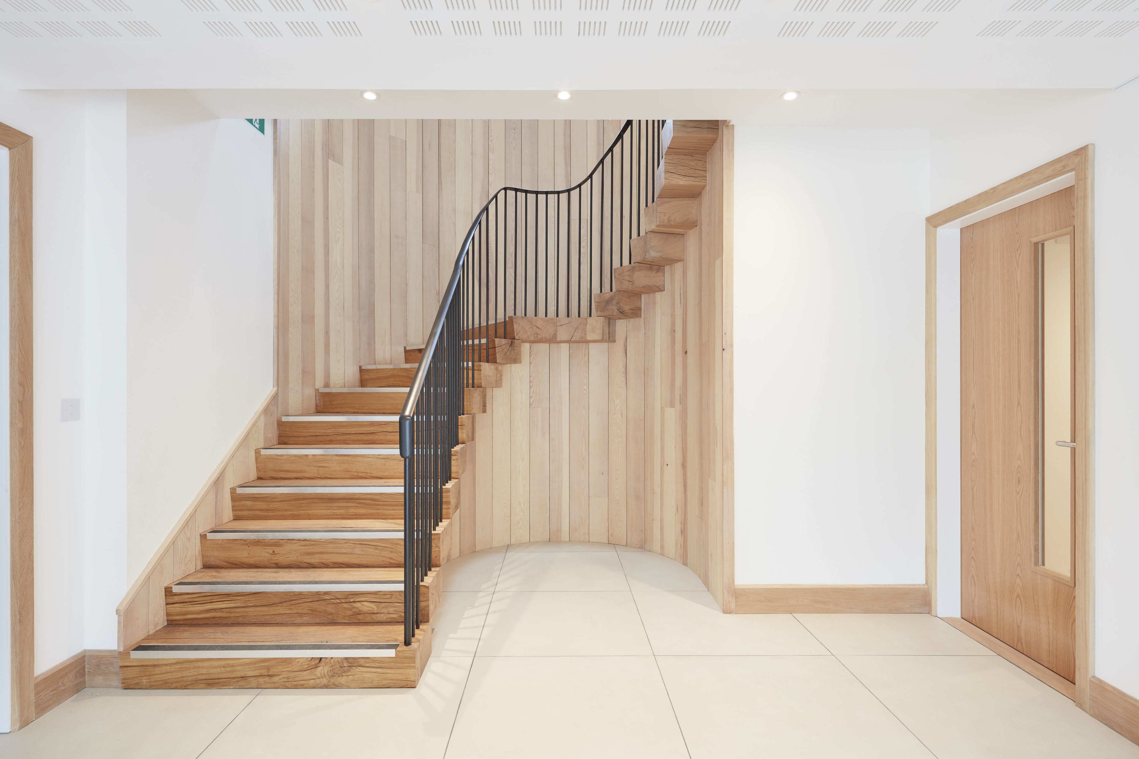 A modern staircase with wooden steps and a metal railing, leading to a door with a wooden frame.