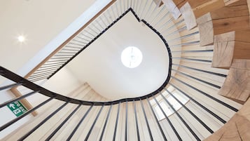A spiral staircase with wooden steps and metal railings, leading to a high ceiling with a skylight.