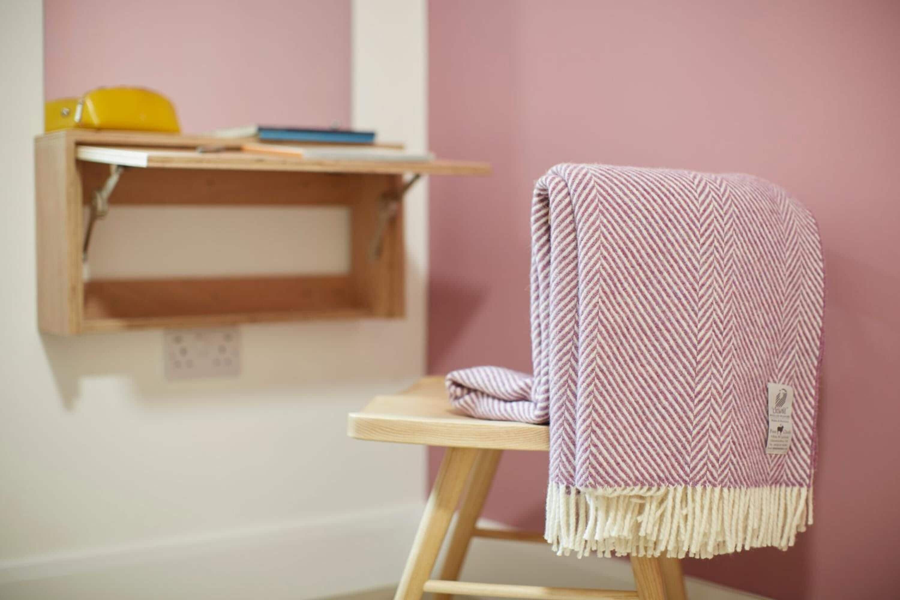 Ein Zimmer mit einem Holztisch, einer rosa Wand und einem Sessel mit gemustertem Überwurf.