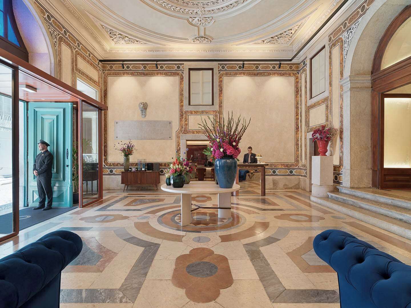 A lobby with a marble floor, a reception desk, and a man standing by the entrance.